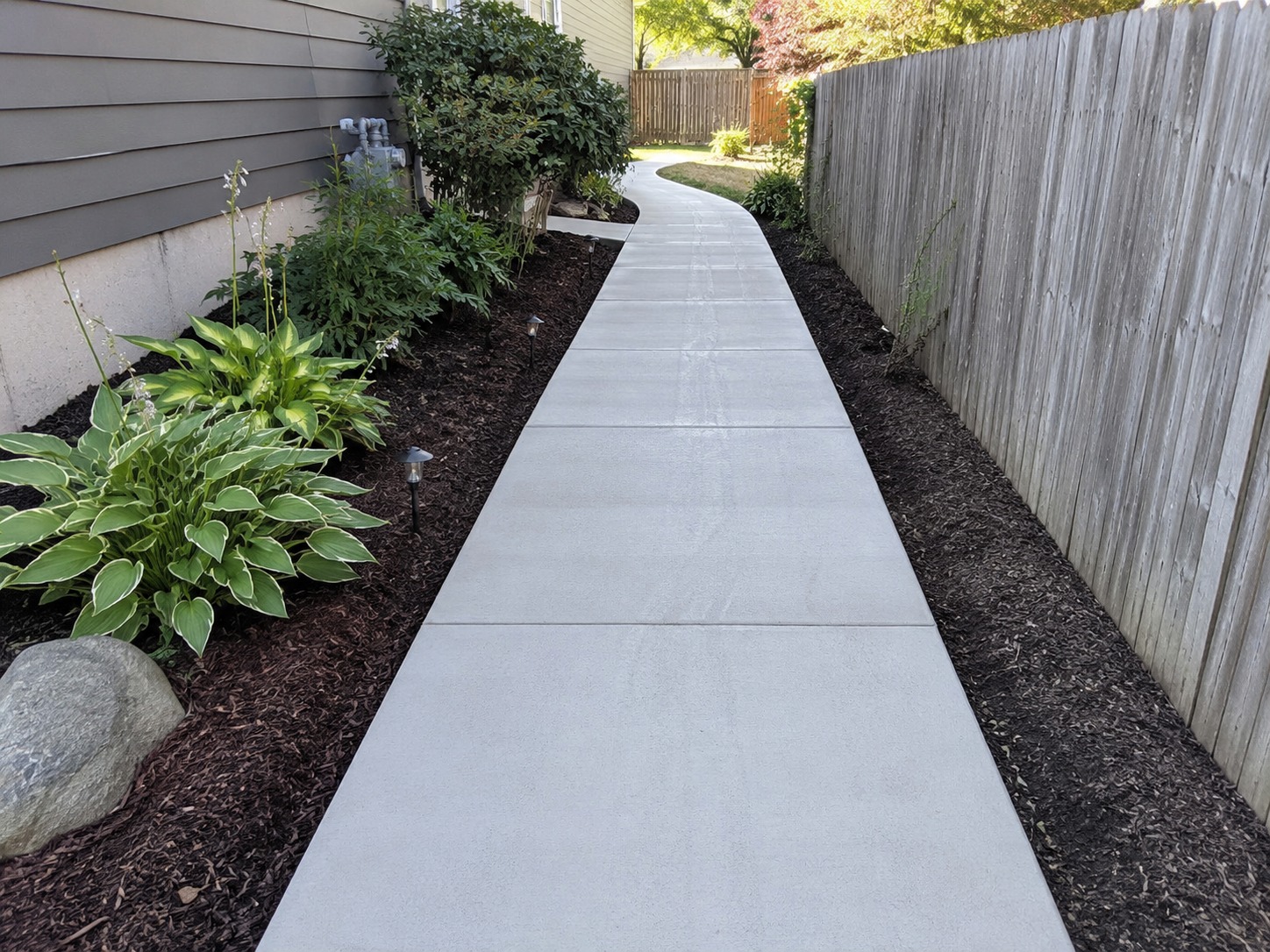 Concrete pathway running alongside a Hamilton home between garden beds