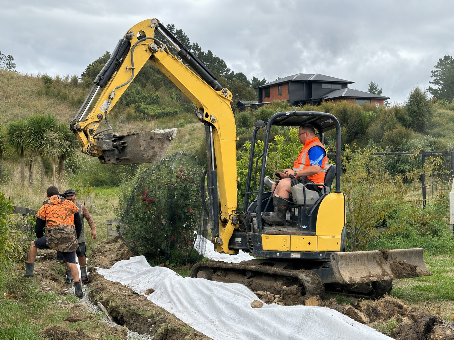 Hamilton concrete crew running a digger while laying drainage on a Waikato property